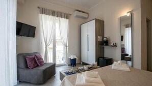 Habitación de hotel con cama, sofá, televisión, armario y balcón con cortinas.