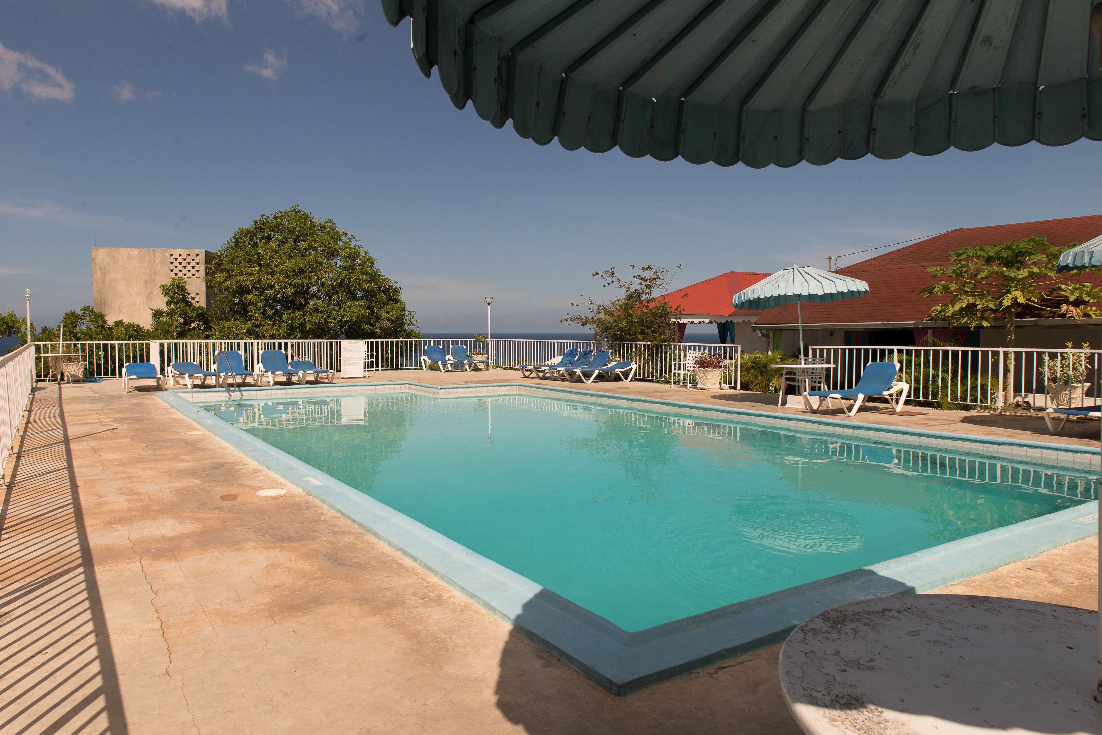 Une piscine rectangulaire bordée de carreaux, entourée de rampes blanches et de chaises longues bleues.
