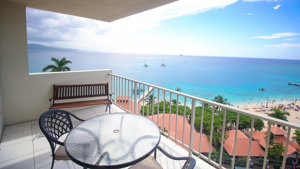 A balcony with a glass table and chairs, overlooking a beach with boats and people. - High Tides Beach Studio (Montego Bay)