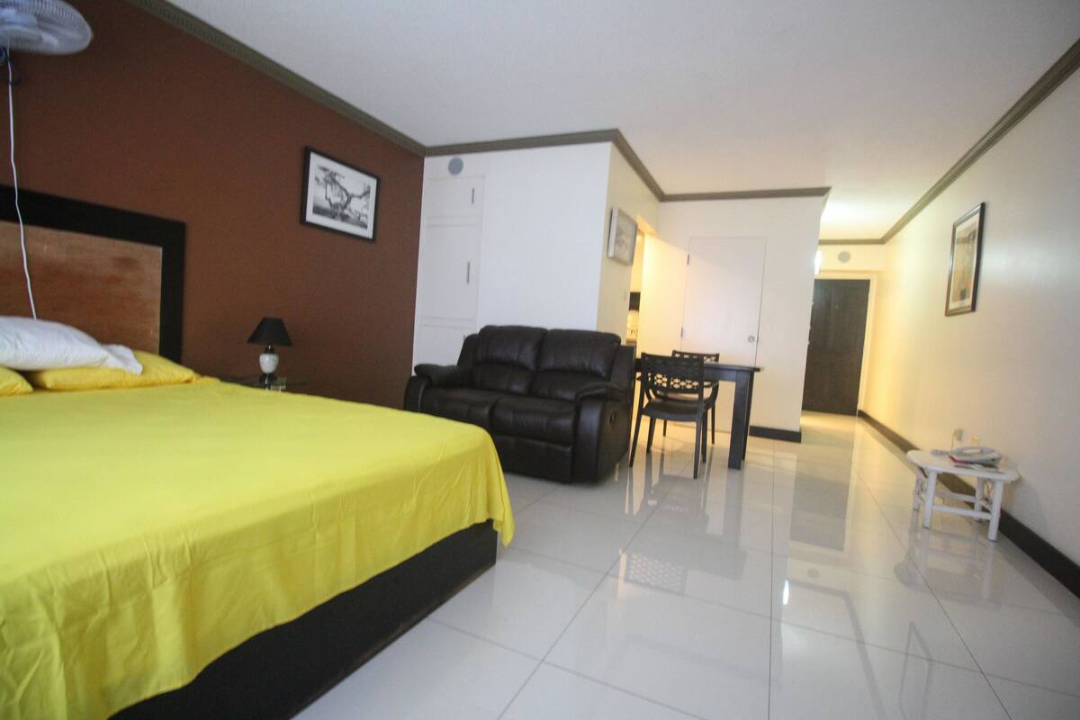 A hotel room with a bed, a black leather sofa, a small table, and a chair.