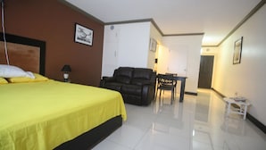 A hotel room with a bed, a black leather sofa, a small table, and a chair. - High Tides Beach Studio (Montego Bay)