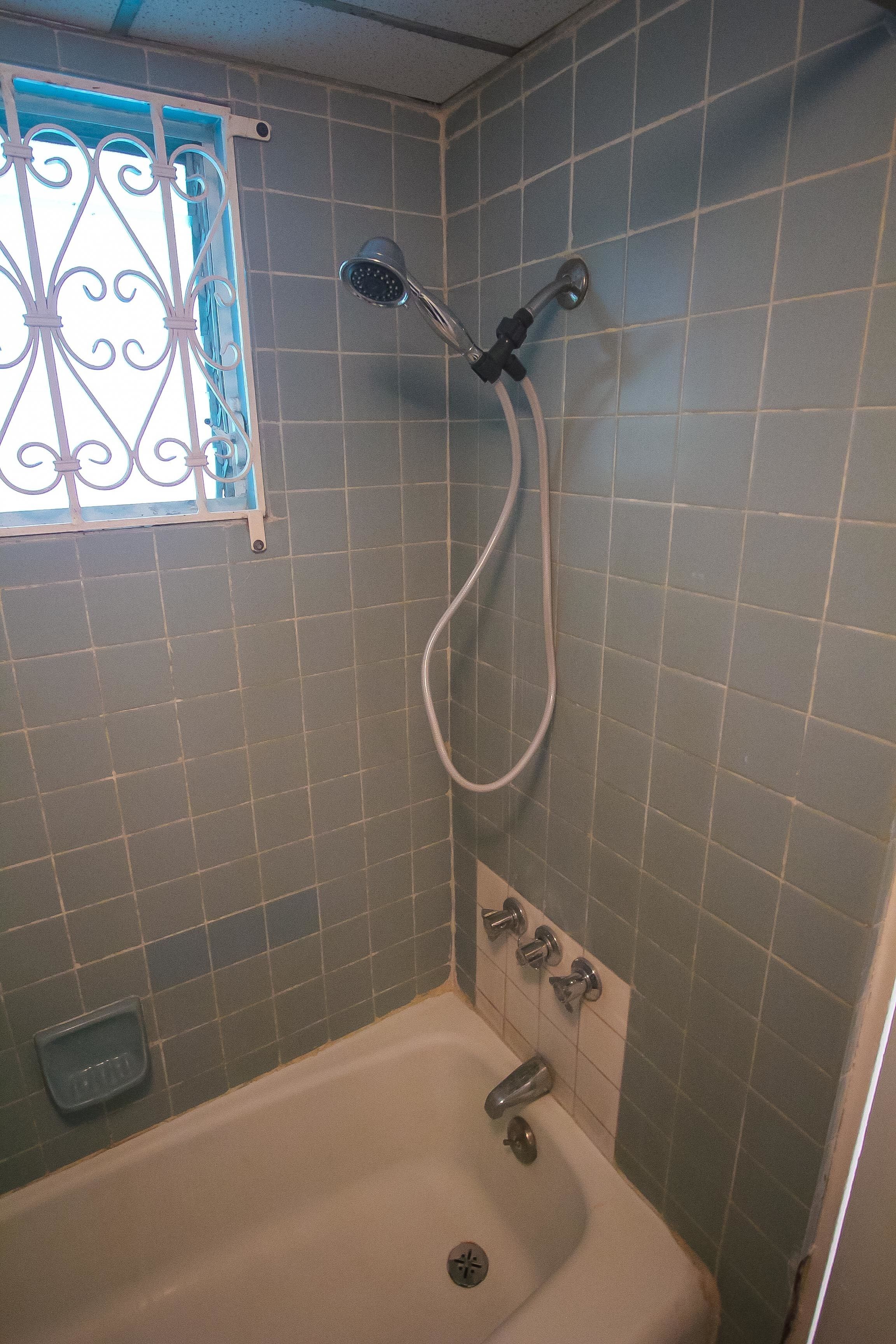 A bathroom with a bathtub, a showerhead, and a window with decorative bars.