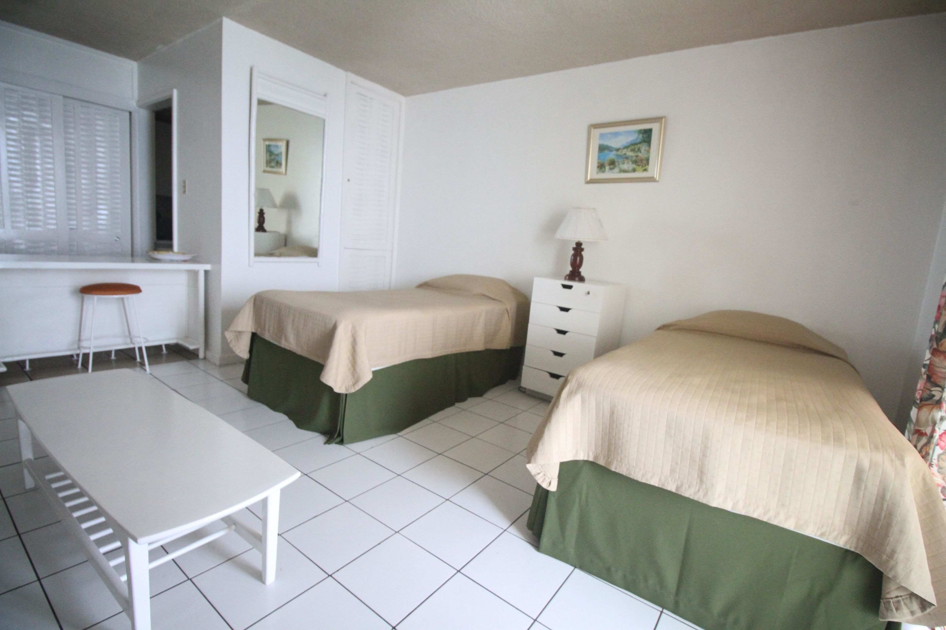A bedroom with two beds, a desk, a chair, and a dresser.