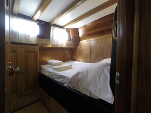 A compact, well-lit bedroom with a single bed, wooden headboard, and a small cabinet.