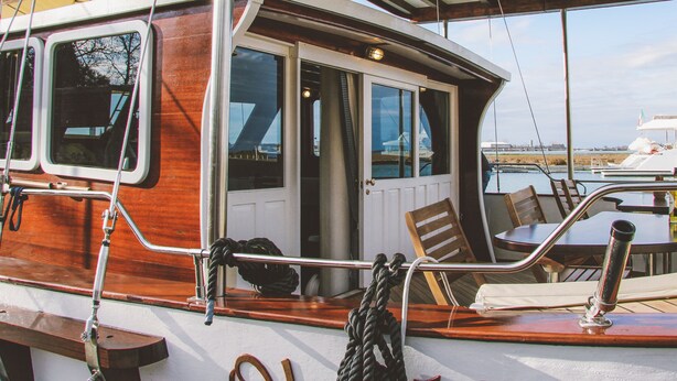 A wooden boat with a cabin, a table with chairs, and a rope tied to the railing. - Veliero Venezia (Venice)