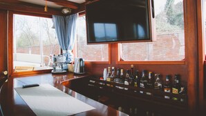 A bar area with a coffee machine, a television mounted above the bar, and a variety of liquor bottles. - Veliero Venezia (Venice)