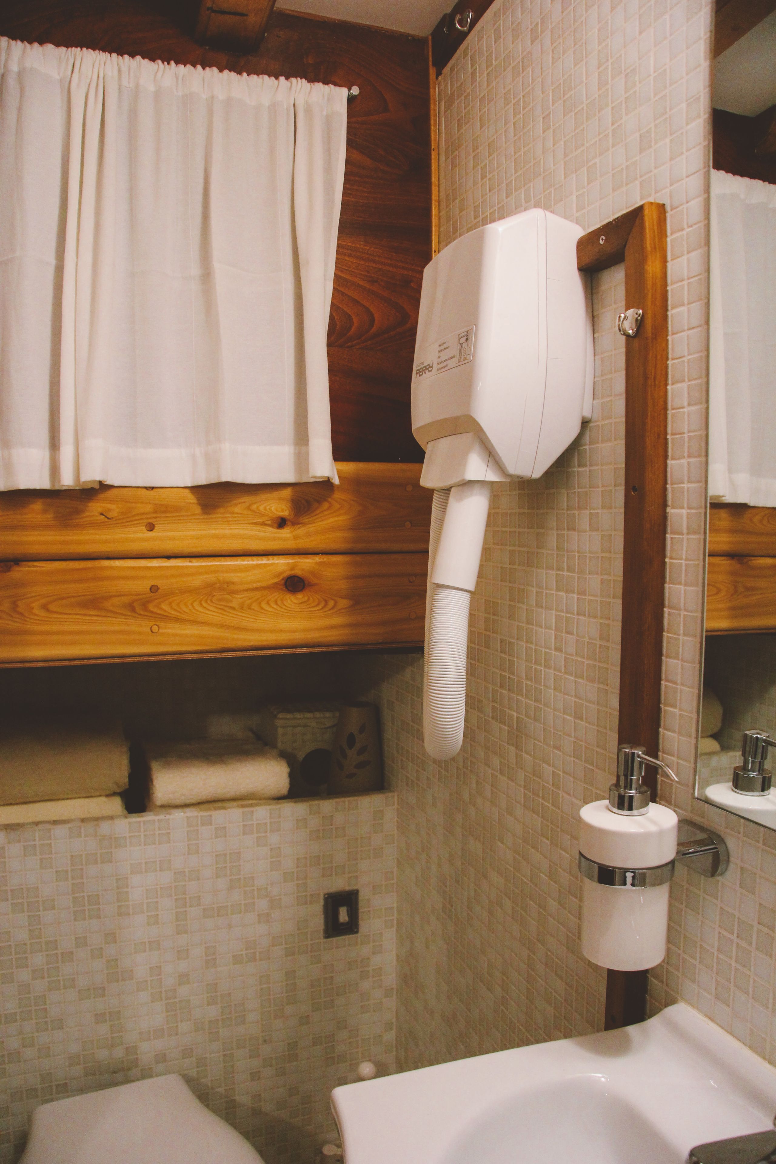 A bathroom with a wooden vanity, a white sink, a towel rack, and a hairdryer mounted on the wall.