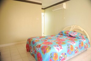 A bedroom with a bed covered in a floral bedspread, a white headboard, and a visible air conditioning unit on the wall.