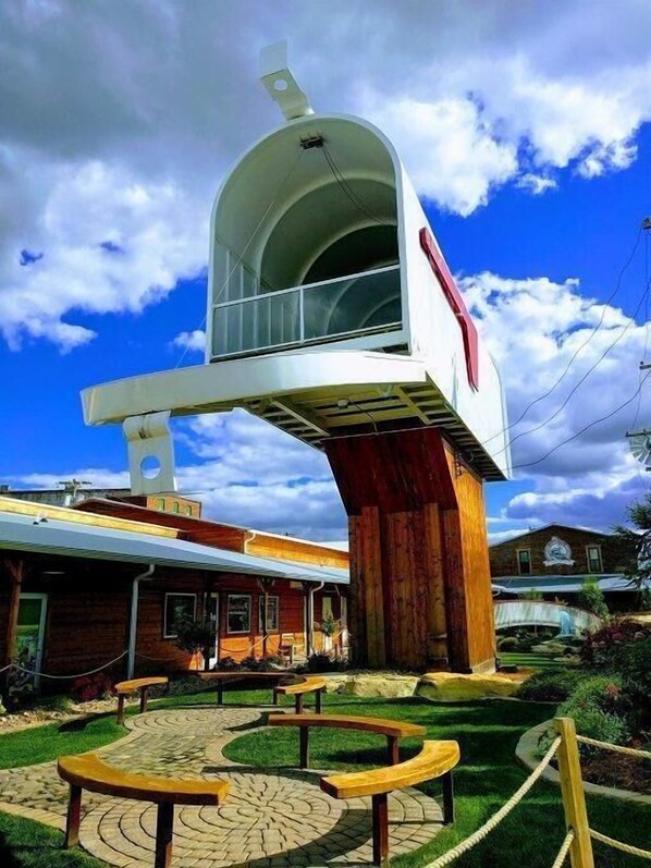 A unique building with a large white structure on top, a wooden base, and a surrounding garden with benches.