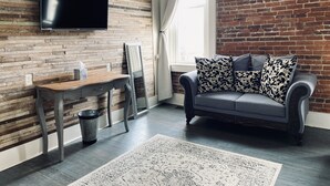 Een moderne woonkamer met een houten wand, een grijze bank en een flatscreen televisie boven een houten bureau.