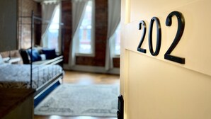 Een hotelkamer met een bed, een bureau en een groot raam met gordijnen. Het kamer nummer is 202.
