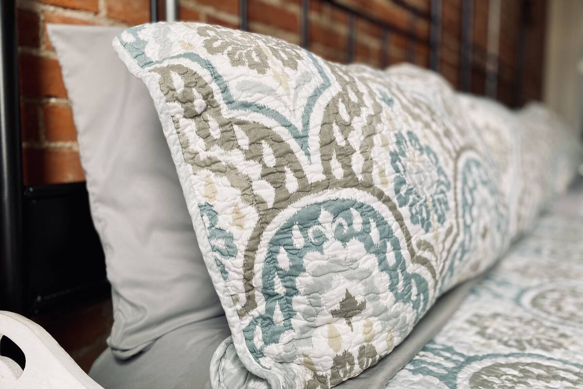 Una cama con colcha y almohadas estampadas frente a una pared de ladrillo.