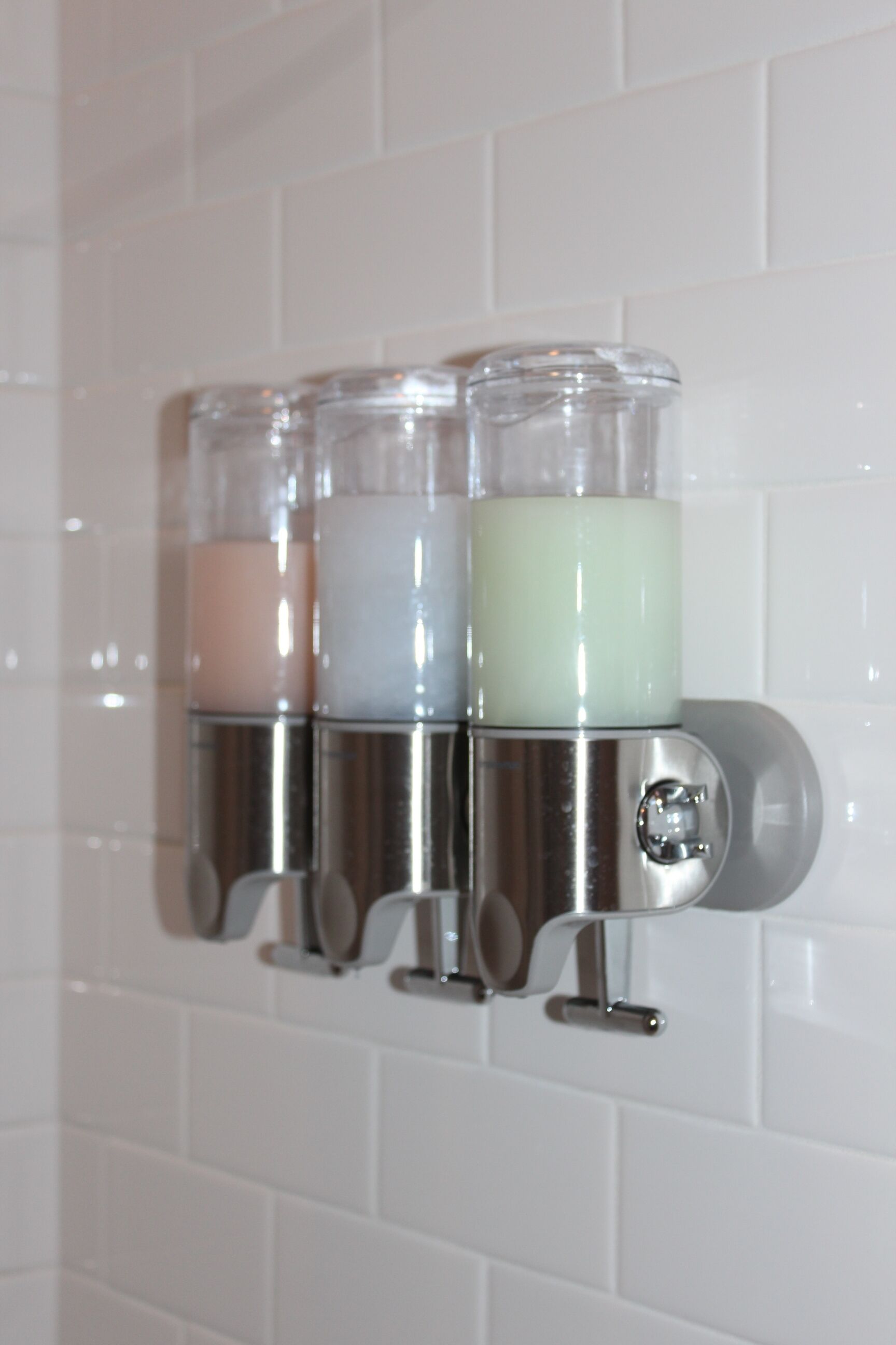 A wall-mounted soap dispenser with three transparent containers, each with a different colored soap.