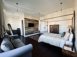 Relax in this serene bedroom featuring a central bed with a white duvet and multiple pillows, a flat-screen TV, and a dresser.