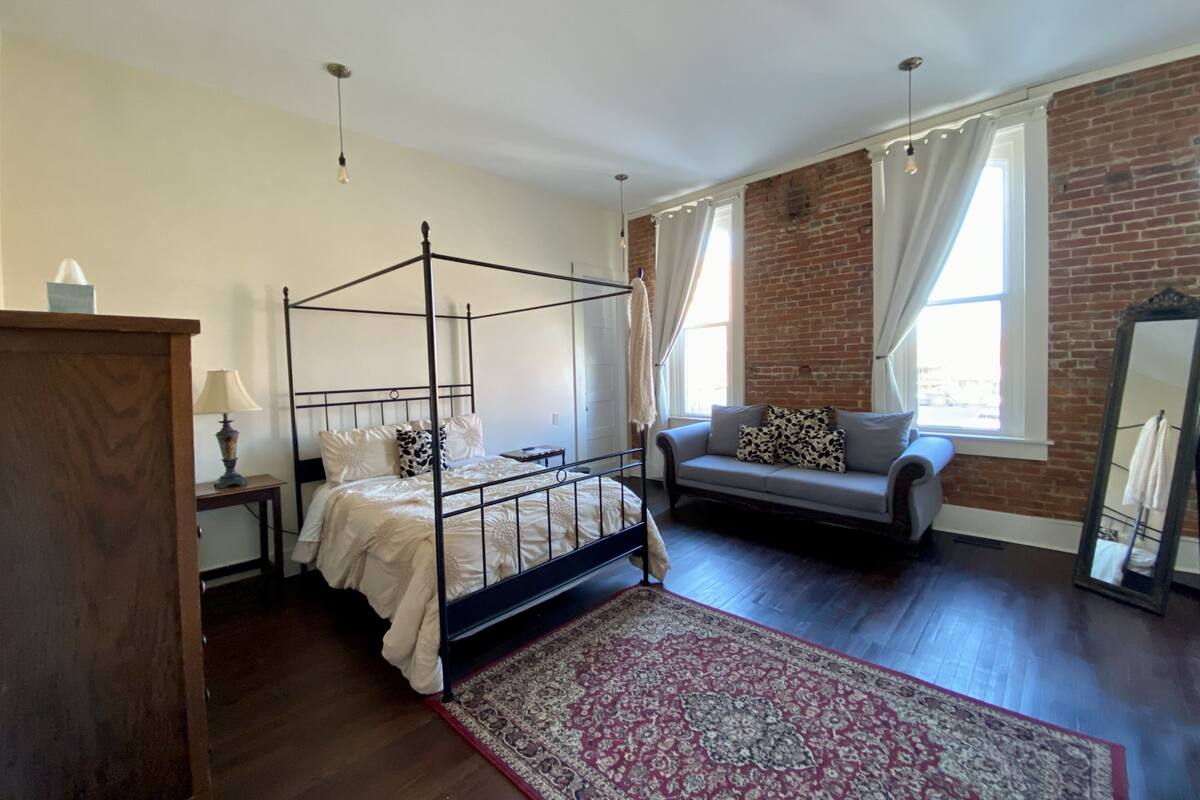 Un dormitorio con una cama con dosel, un sofá, un espejo y una pared de ladrillo.