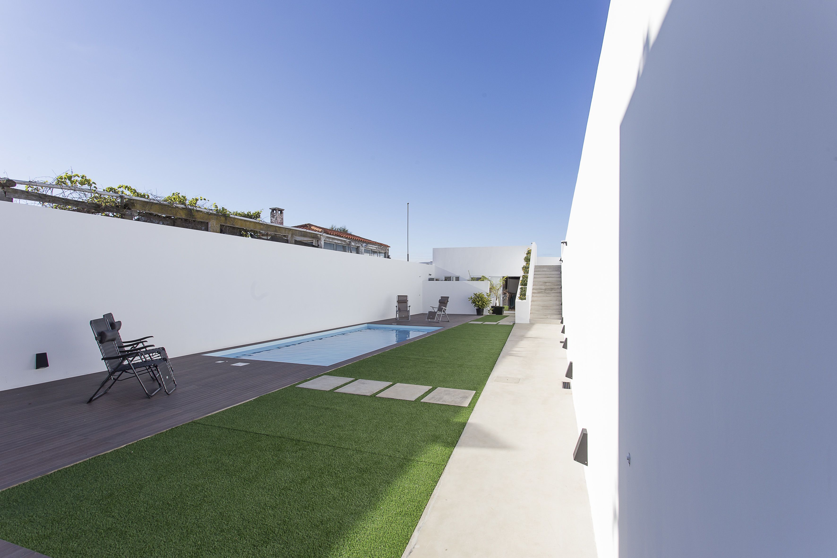 A modern outdoor space with a swimming pool, artificial grass, and a white wall.