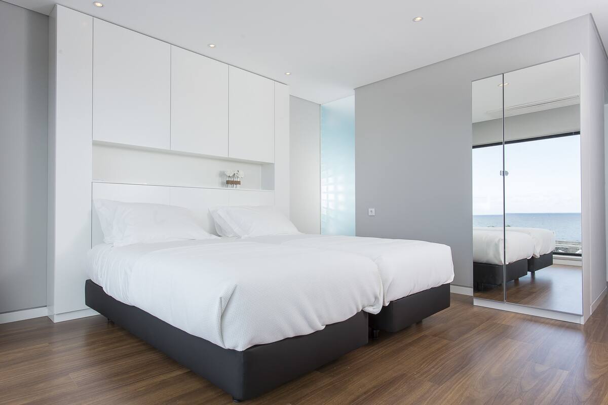 Quarto moderno com cama grande, armário embutido e vista para o mar.