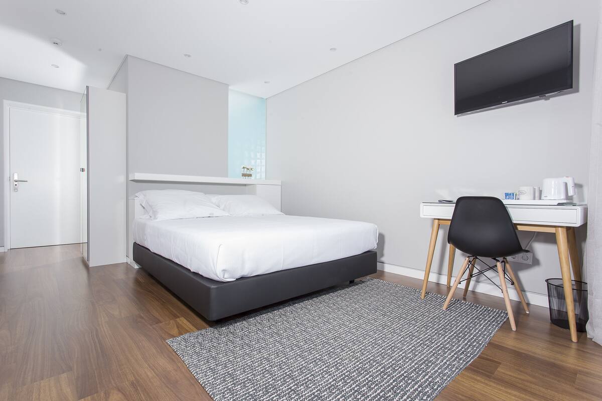 Quarto de hotel moderno com cama, escrivaninha, cadeira e televisão de tela plana.