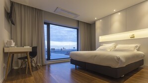 A modern hotel room with a large bed, a desk, and a view of the cityscape through a large window. - Praia de Santos - Exclusive Guest House (Ponta Delgada)