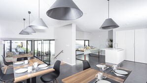 A modern dining area with a wooden table set for four, black chairs, and pendant lighting. - Praia de Santos - Exclusive Guest House (Ponta Delgada)
