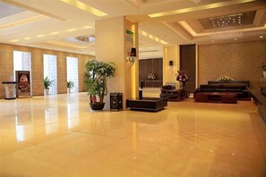 Eine geräumige Lobby mit poliertem Boden, einem Empfangstisch, einer Sitzecke mit Sofas und einer großen Topfpflanze.
