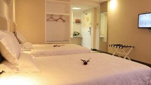 Ein Hotelzimmer mit zwei Betten, einem an der Wand befestigten Fernseher und einem kleinen Tisch mit einem Stuhl.