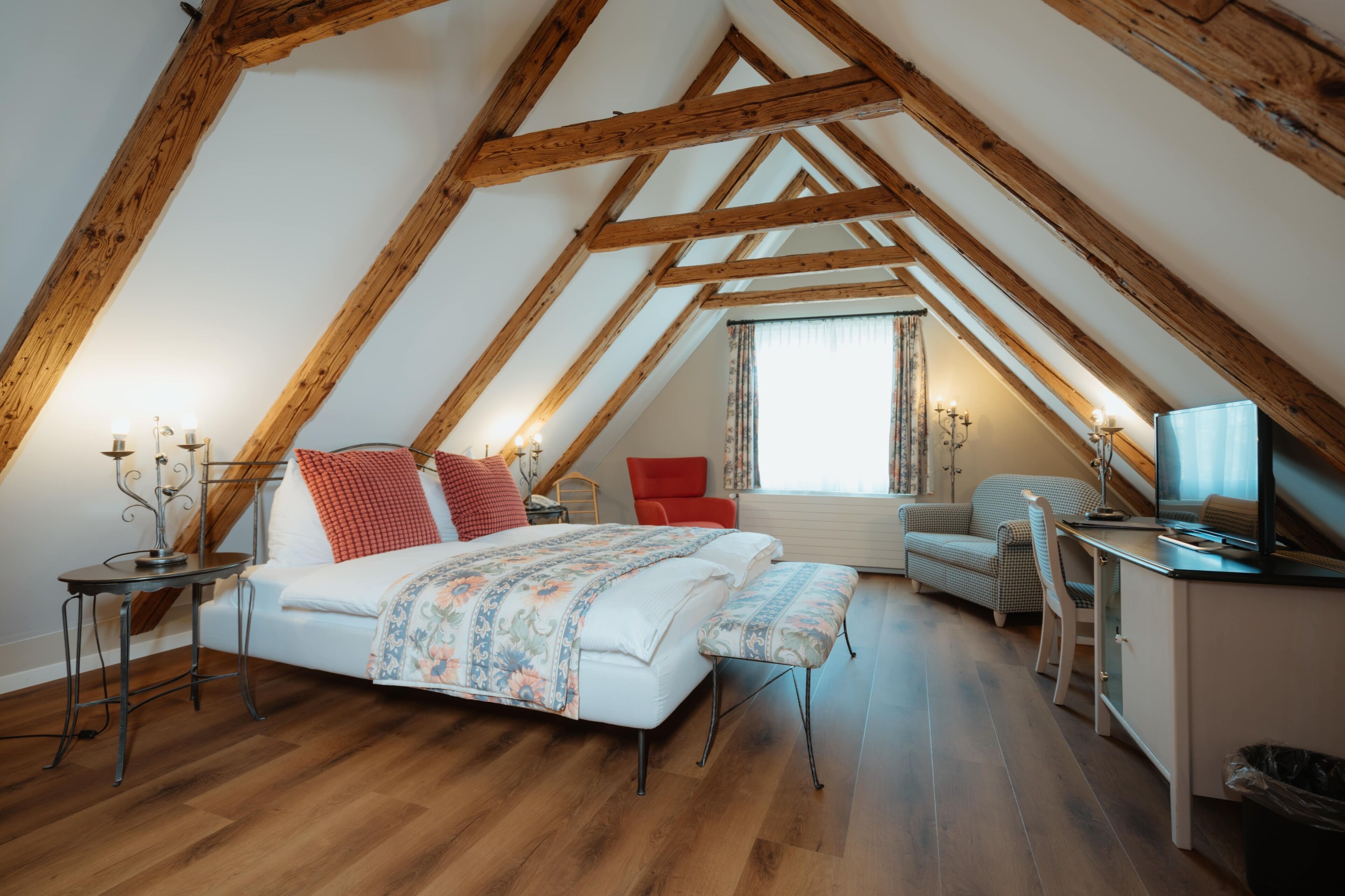 Un dormitorio con techo inclinado, una cama con colcha estampada, un escritorio con computadora y una silla.