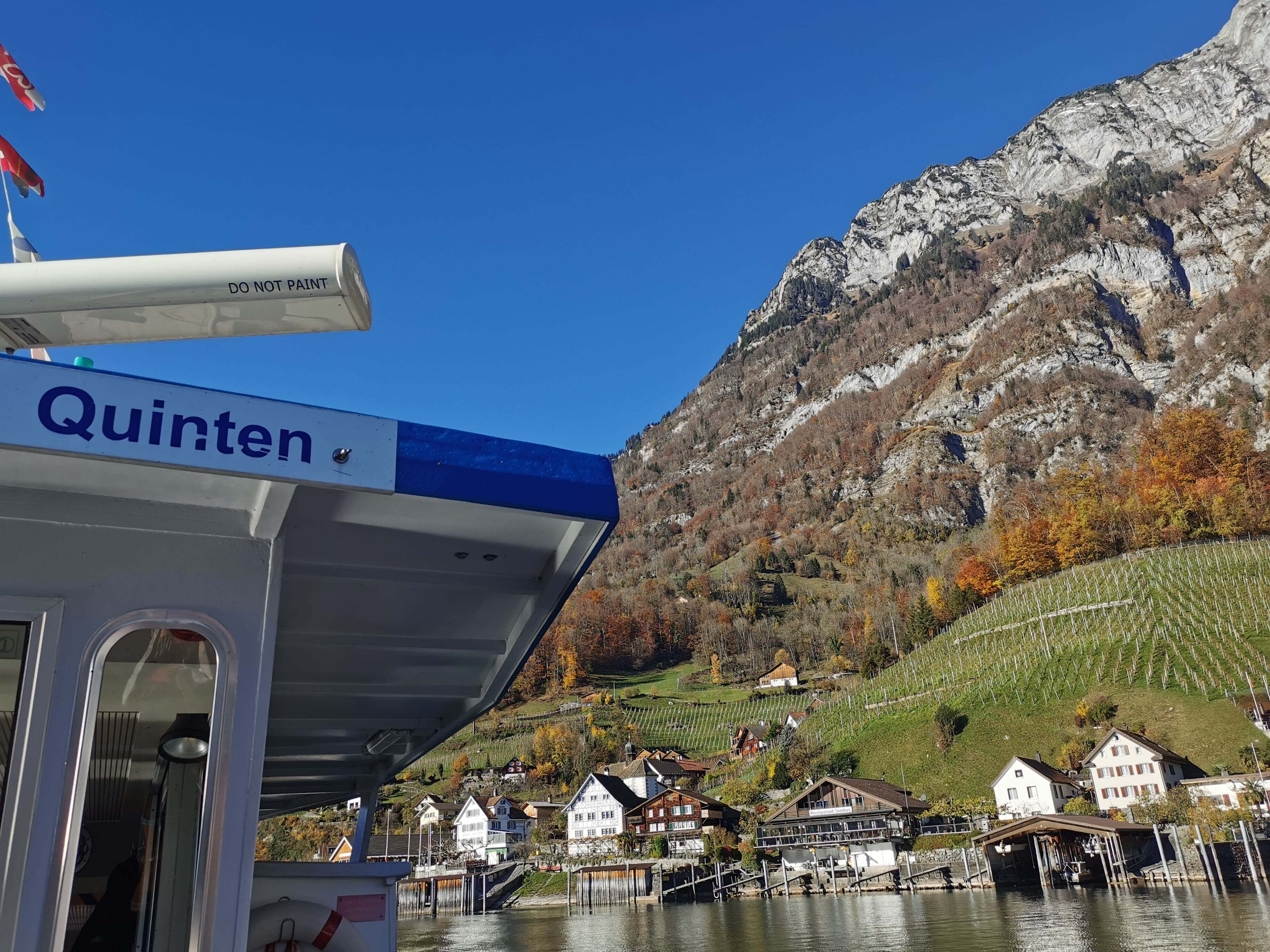 A boat with a 'Quinten' sign, docked near houses and a mountain backdrop.
