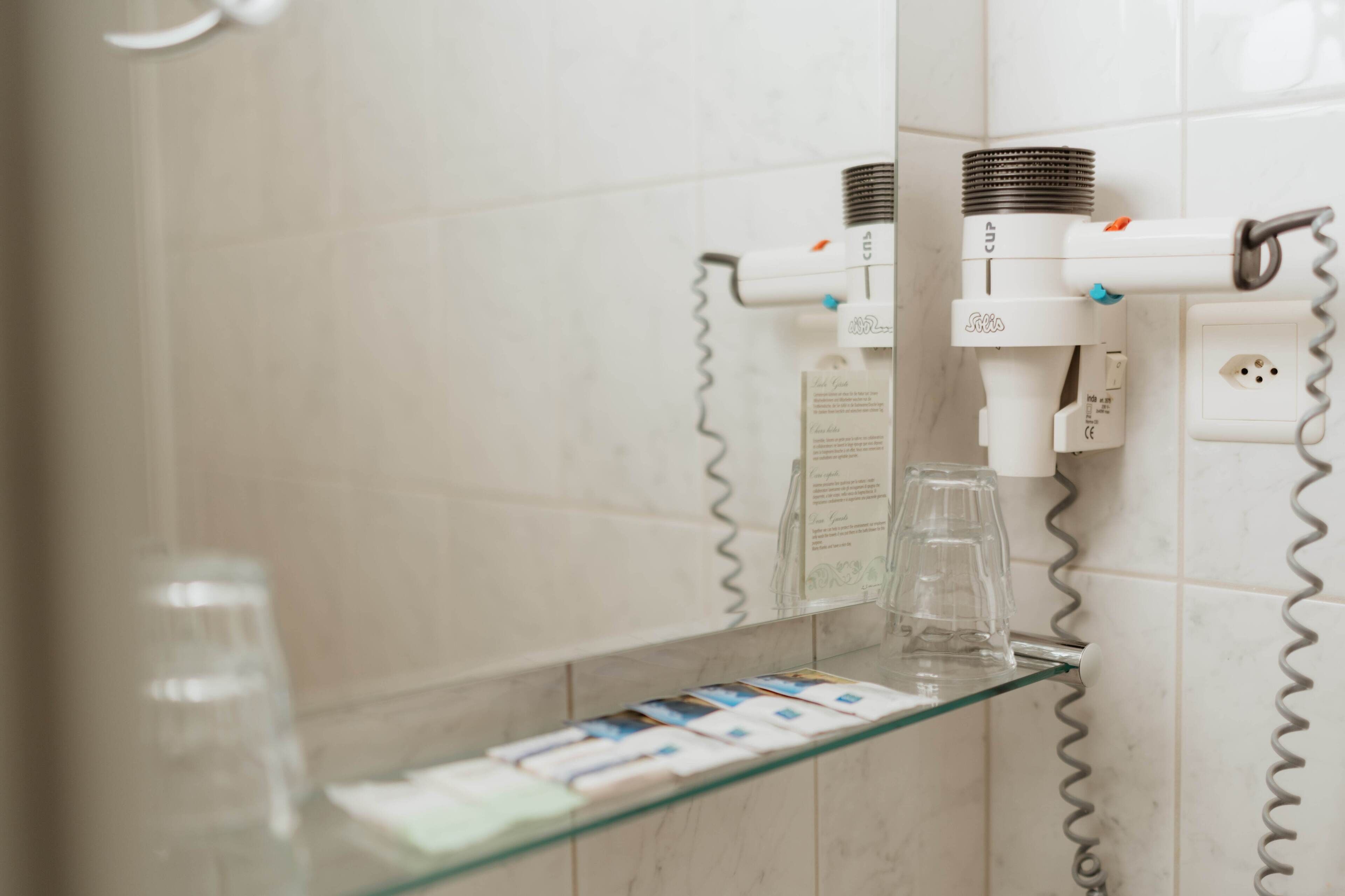 Ein Badezimmer mit einer Glasablage für Toilettenartikel und einem Föhn auf einem an der Wand befestigten Ablagebrett.