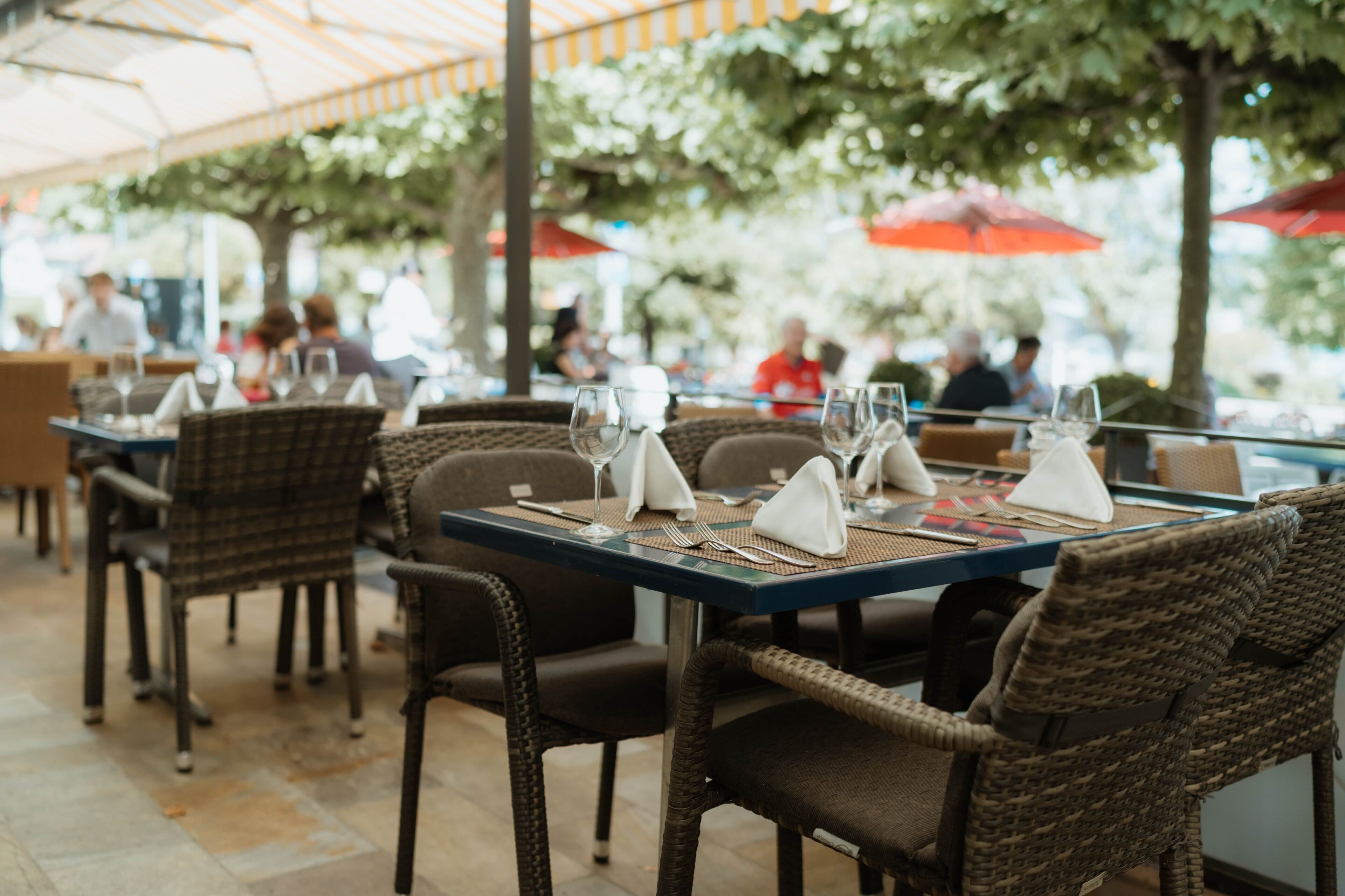 An outdoor dining area with wicker chairs and tables set up under a striped canopy.