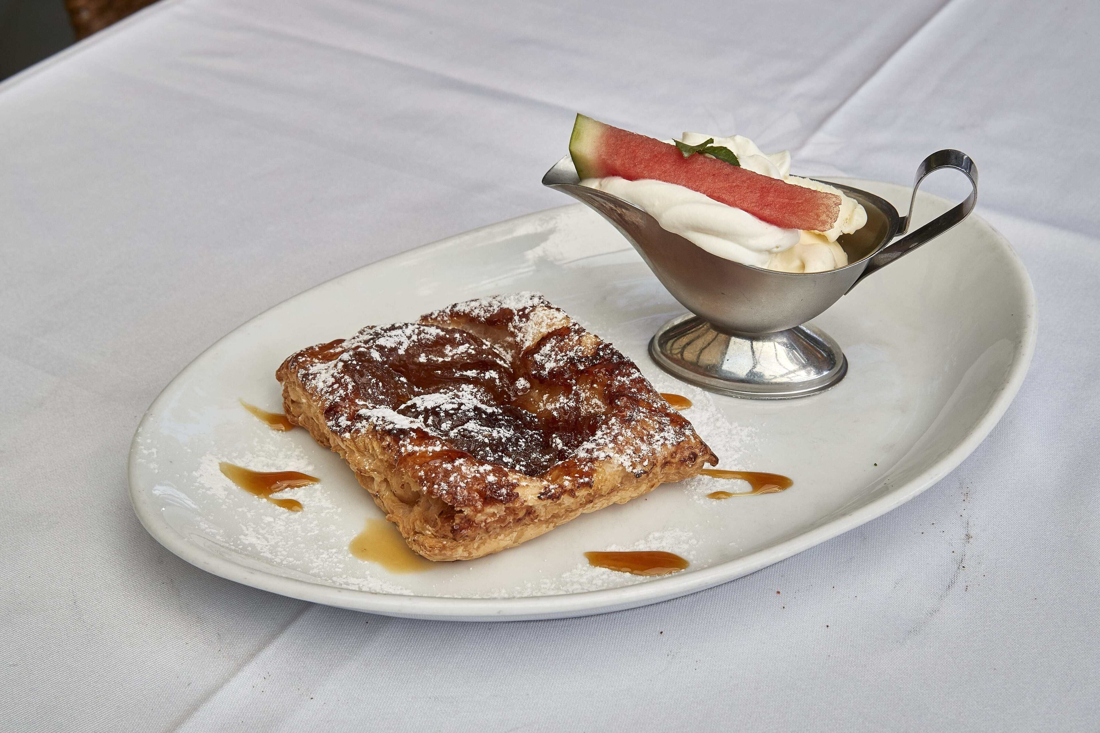 Une assiette à dessert avec une pâtisserie et un petit bol de crème fouettée et de fruits.