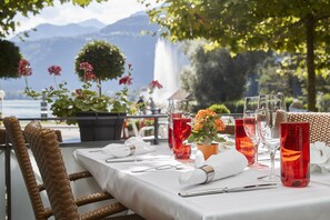 A table set for dining with a view of a lake and mountains, including a wicker chair and a white tablecloth. - Parkhotel Schwert - Self-Check-in (Weesen)