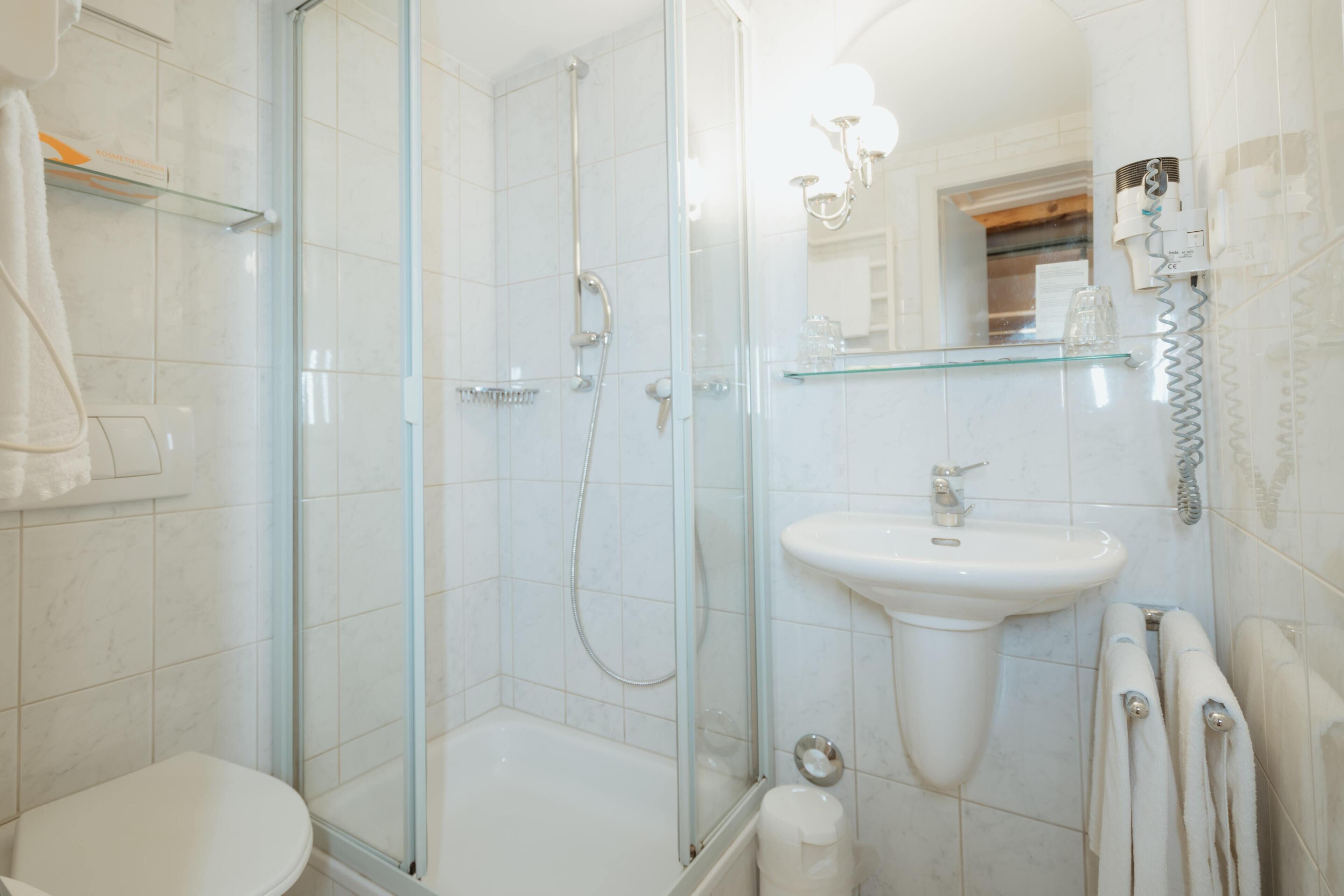 Ein modernes Badezimmer mit einer gläsernen Duschkabine, einem weißen Waschbecken und einem Spiegel.