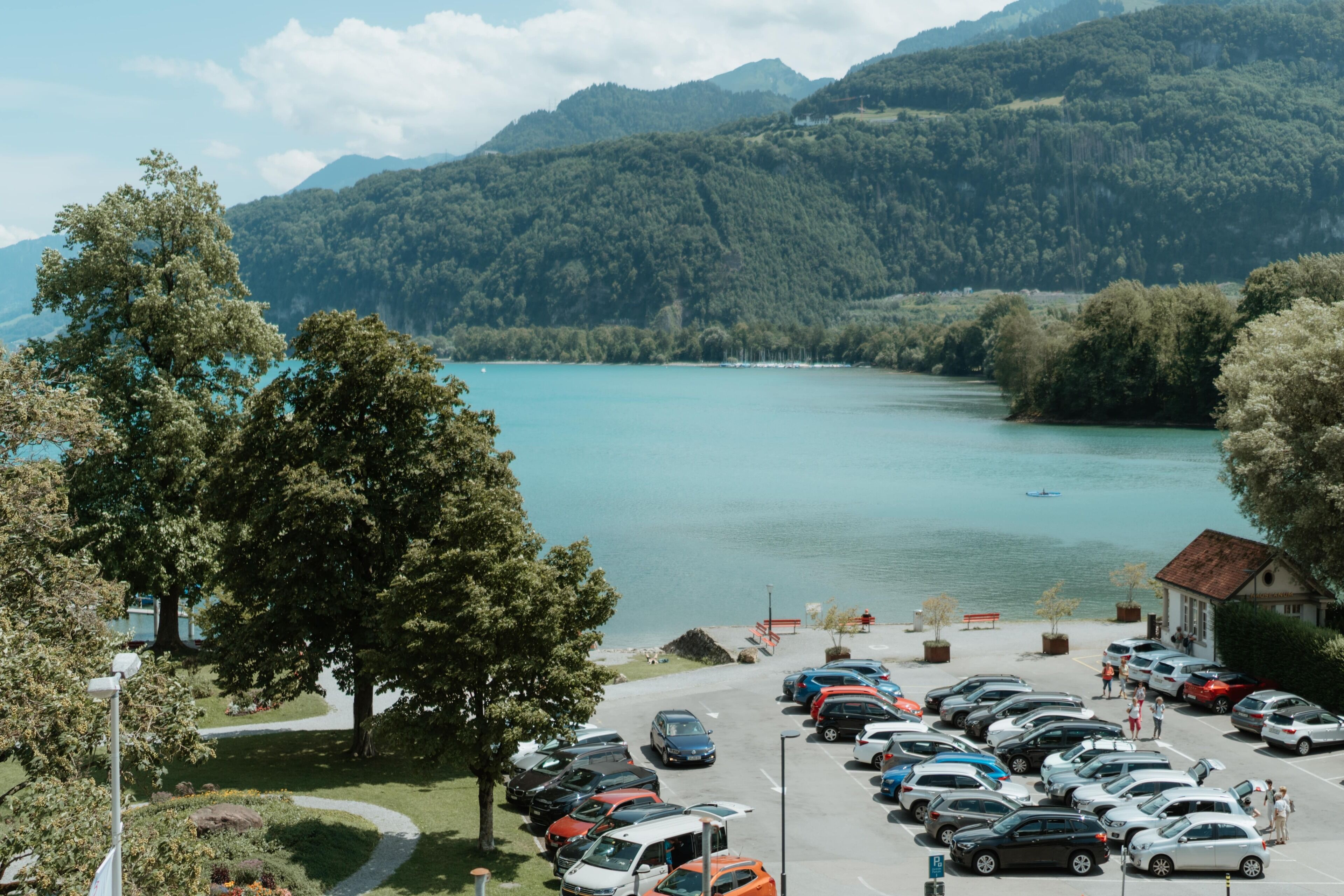 A parking lot with cars, a building, and a lake with mountains in the background.