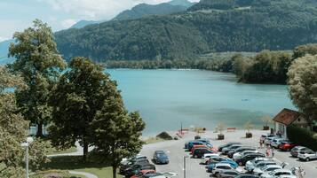 A parking lot with cars, a building, and a lake with mountains in the background.