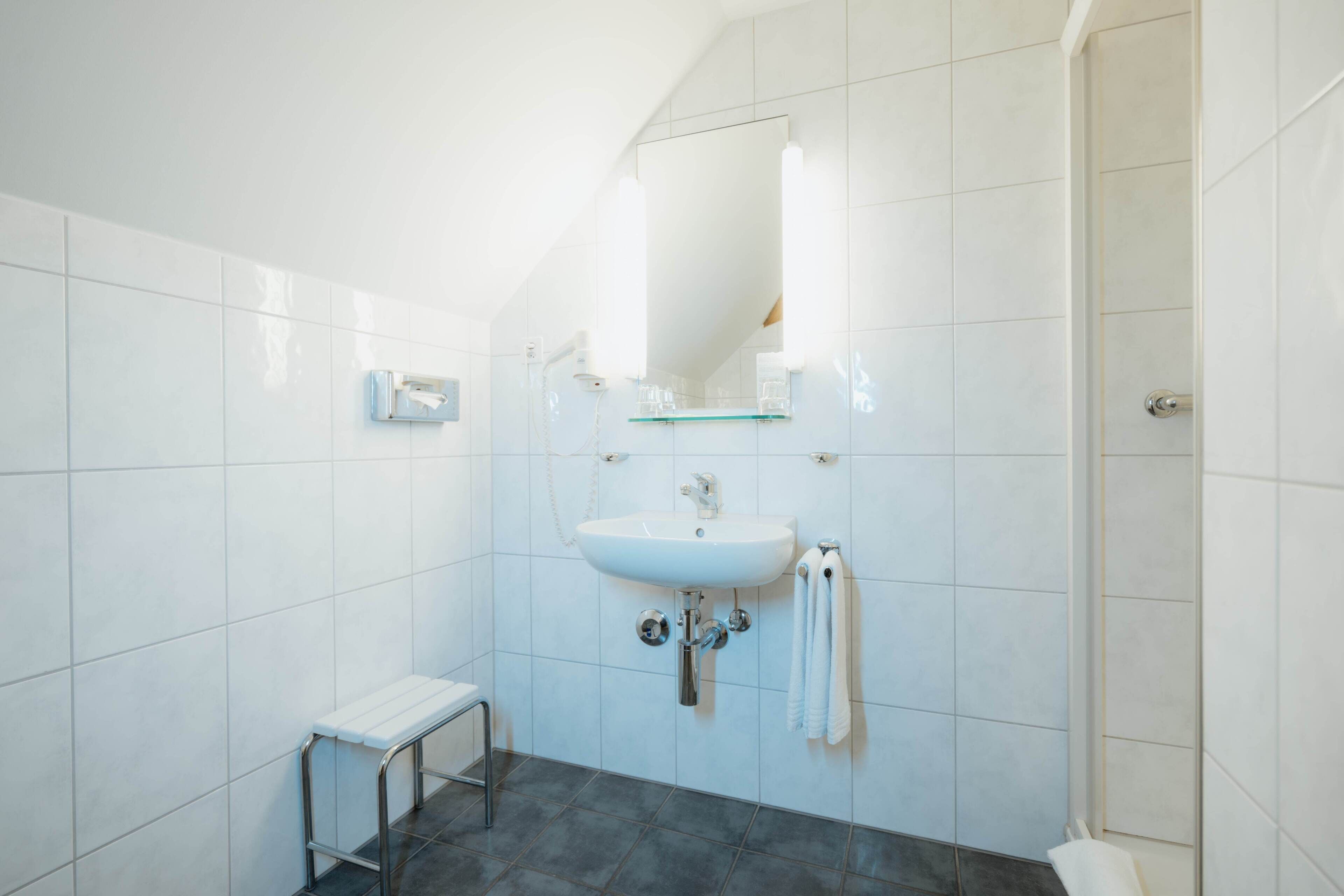 Ein Badezimmer mit weißen Fliesen, einem Waschbecken, einem Spiegel und einer Dusche.