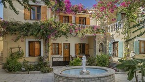 A courtyard with a fountain, a pool, and a building with wooden shutters and flowering vines. - Olympia Village (Samos)