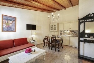 Una sala de estar acogedora con un sofá rojo, una mesa de comedor con sillas, una araña y una zona de cocina con armarios blancos.