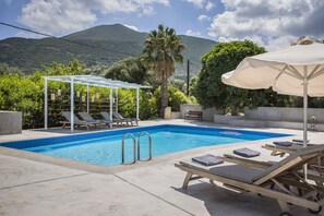A swimming pool with lounge chairs and a pergola, surrounded by greenery and mountains. - Emily Villas (Kefalonia)