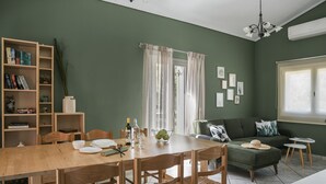 A dining area with a wooden table and chairs, a bookshelf, and a green sofa. - Emily Villas (Kefalonia)