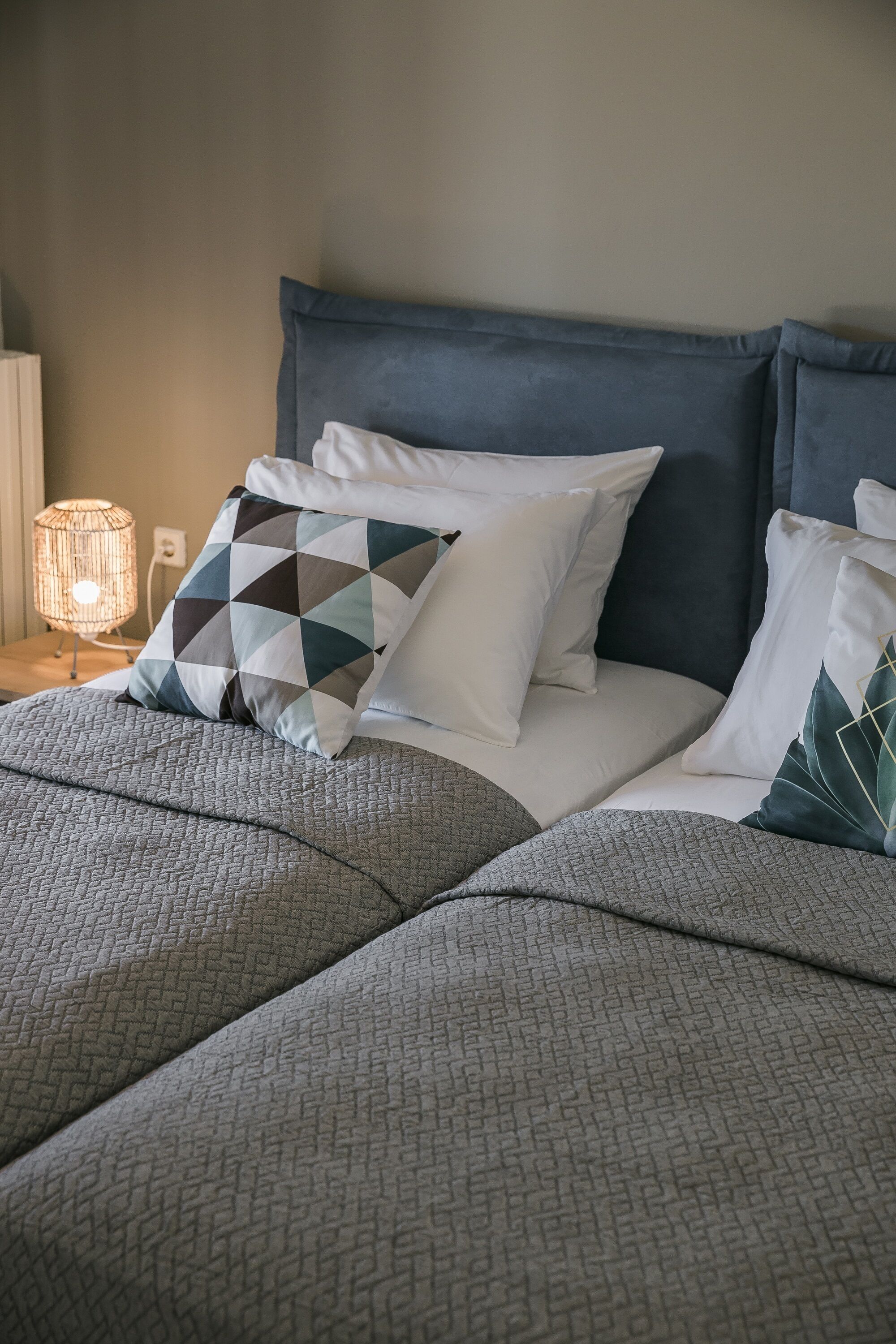 A neatly made bed with a patterned bedspread, a geometric pillow, and a bedside lamp.