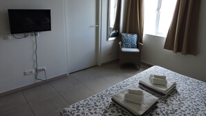 Ein Hotelzimmer mit Bett, Sessel, Wandfernseher und einem Fenster mit Vorhängen.