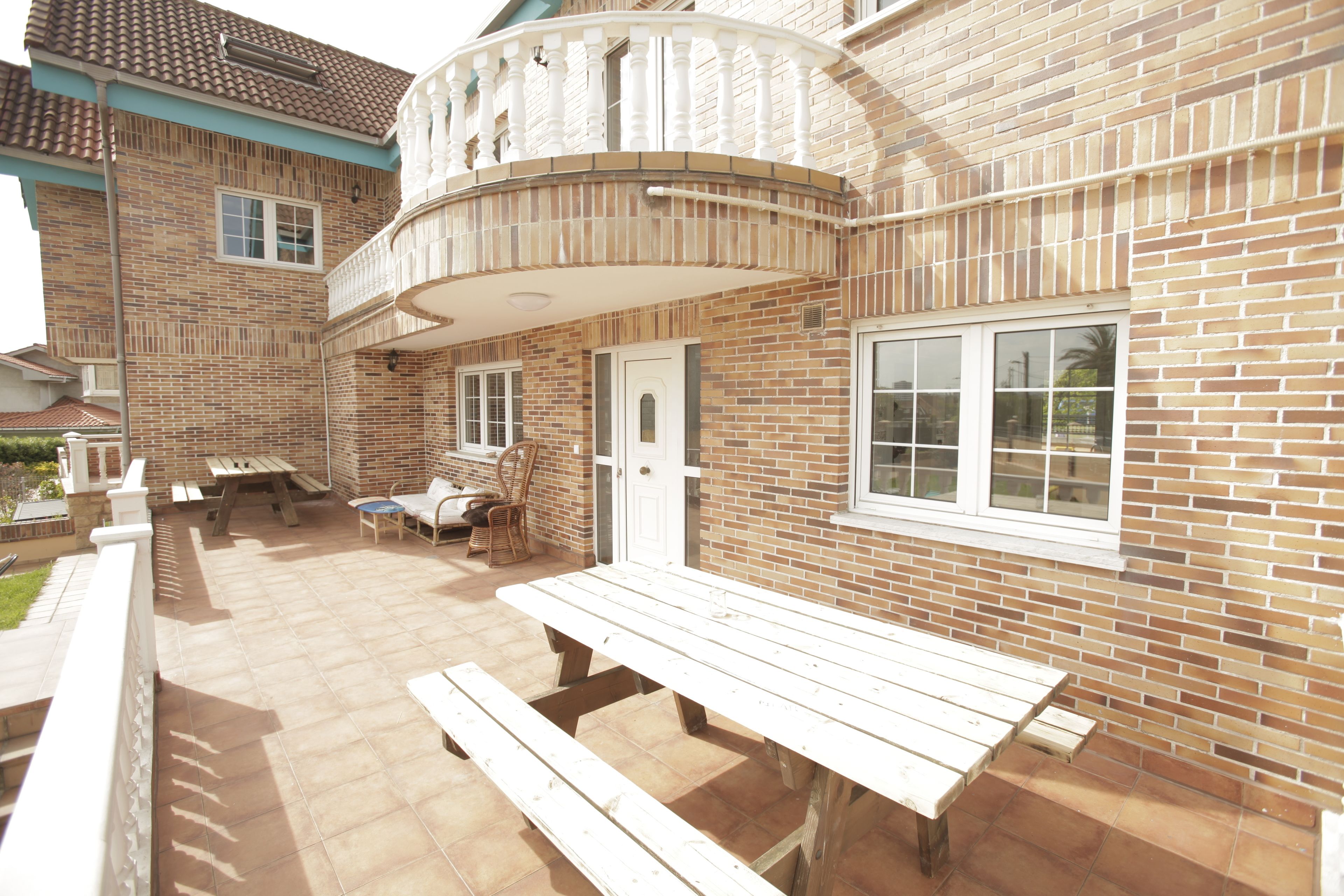 A patio area with a wooden table and benches, a brick wall, and a window.