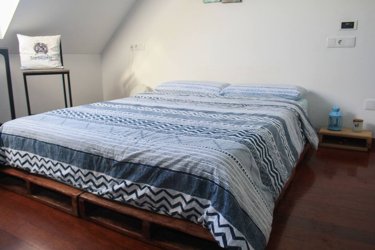 A bedroom with a bed, a pillow with a logo, a nightstand, and a wall socket.