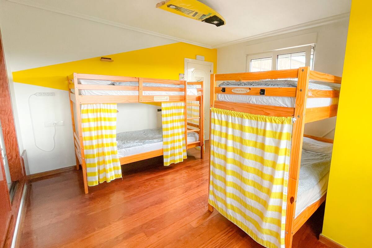 A room with three bunk beds, wooden flooring, and yellow walls.