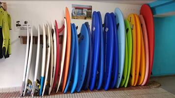 Una hilera de tablas de surf contra una pared, con un cartel que indica que el uso de equipo de protección es obligatorio.