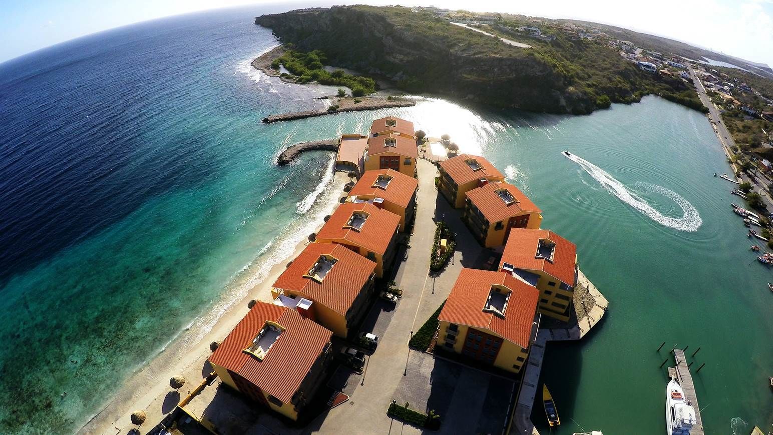 Vista aérea de un hotel costero con varias edificaciones, una playa y un puerto deportivo.