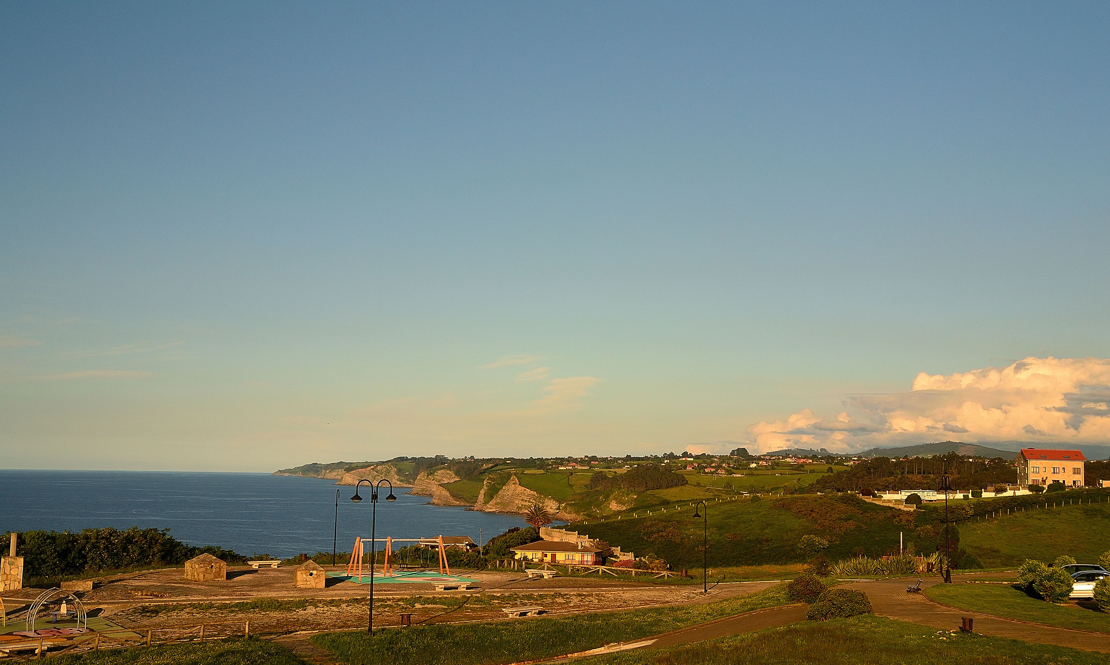 Un paysage côtier avec vue sur la mer, un petit village et un grand bâtiment doté d’un toit rouge.