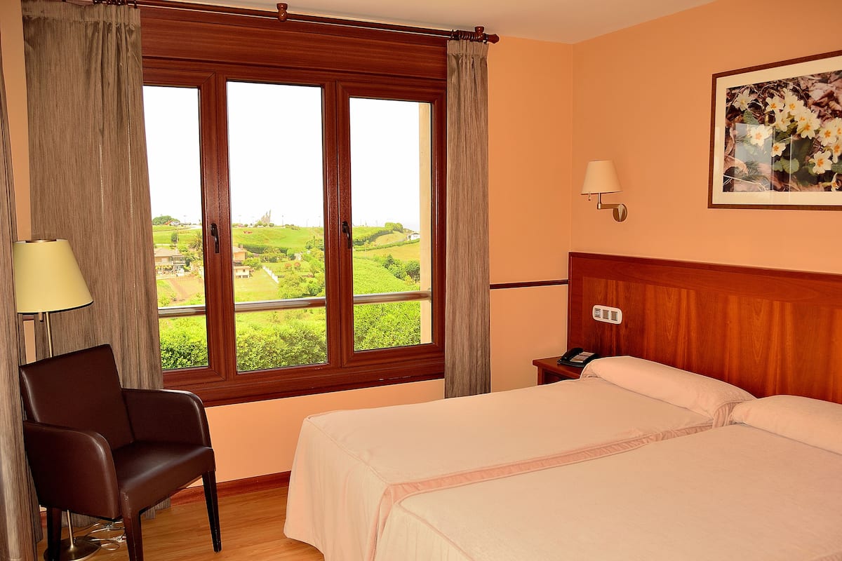 A hotel room with a large window, a chair, a bedside table, a lamp, and a bed.