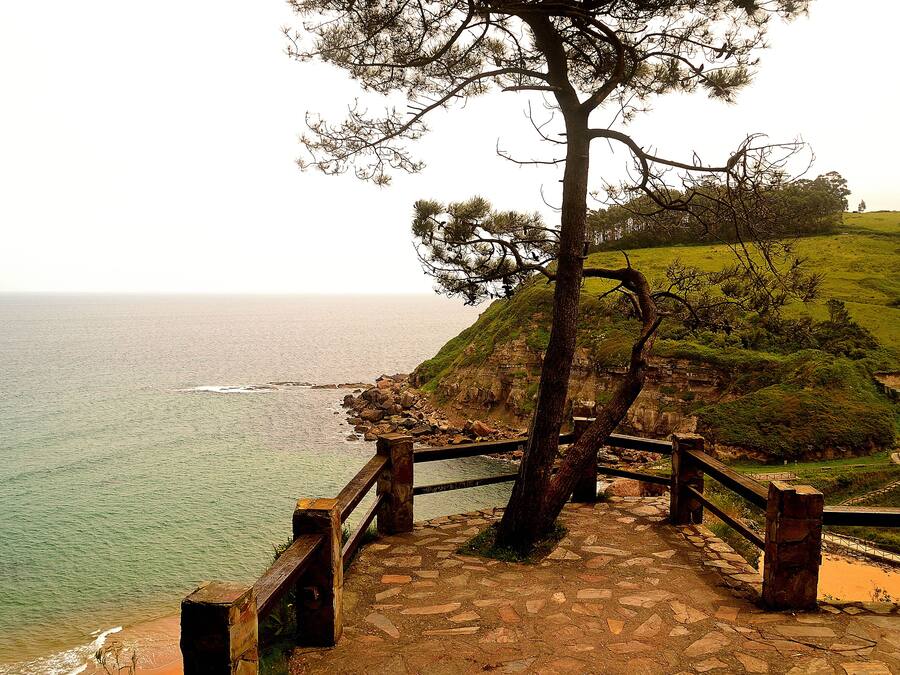 Una escalera de piedra que lleva a un mirador costero con barandilla de madera y vista al mar.